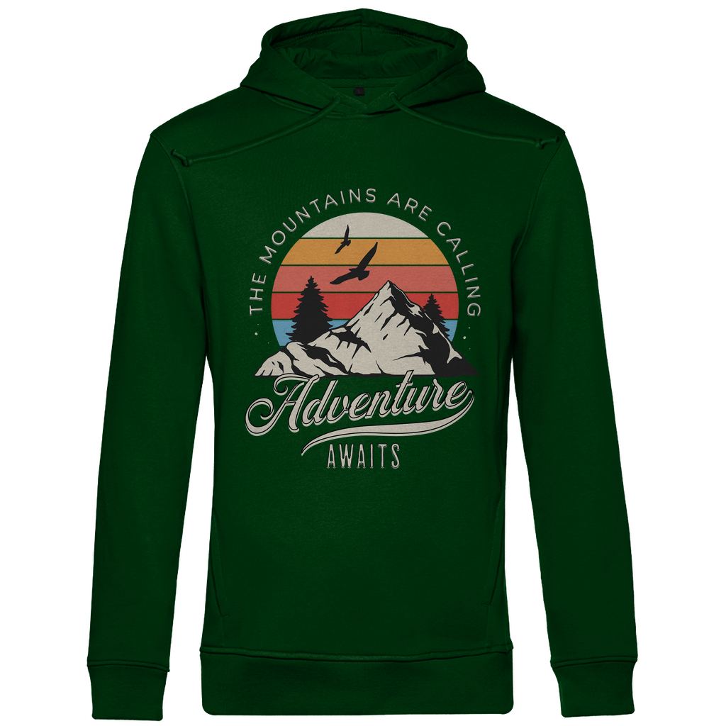 Ein grüner Hoodie mit einem Outdoor-Design, das einen Berg, Bäume und fliegende Vögel zeigt. Im Hintergrund ist ein Sonnenuntergang in warmen Farbstreifen abgebildet. Der Text "The Mountains Are Calling" ist im oberen Bereich des Designs zu sehen, während "Adventure Awaits" in geschwungener Schrift darunter steht. Das Design vermittelt eine abenteuerliche und naturverbundene Atmosphäre, ideal für Liebhaber von Outdoor-Aktivitäten und Bergen.