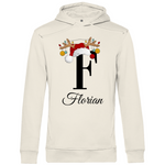 Ein cremefarbiger Hoodie mit einem weihnachtlichen Design, das den Buchstaben "F" zeigt. Der Buchstabe ist in schwarz gehalten und mit einem Weihnachtsmann-Hut sowie Rentiergeweihen verziert, an denen bunte Kugeln hängen. Unter dem Buchstaben ist der personalisierte Name "Florian" in eleganter, geschwungener Schrift zu sehen. Der Hoodie strahlt eine festliche und personalisierte Stimmung aus und eignet sich perfekt für die Winter- und Weihnachtszeit.