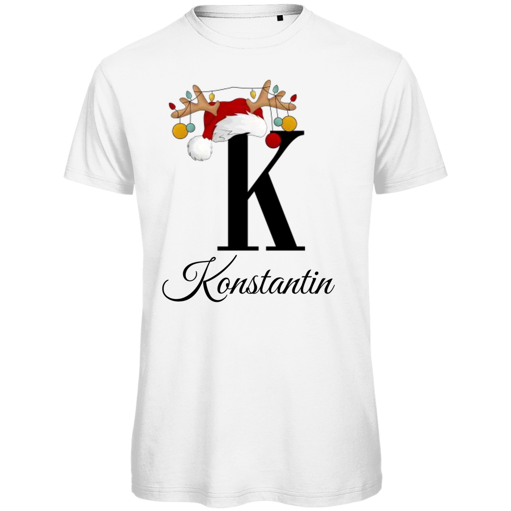 Ein weißes T-Shirt mit einem weihnachtlichen Design. Der große Buchstabe "K" ist mittig auf der Brust abgebildet und trägt einen Weihnachtsmann-Hut sowie Rentiergeweihe, an denen bunte Weihnachtskugeln hängen. Unterhalb des Buchstabens steht der Name "Konstantin" in eleganter, geschwungener Schrift. Das Design vermittelt eine festliche Stimmung und ist personalisiert für den Namen Konstantin.