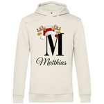 Ein cremefarbener Hoodie mit einem festlichen Design. Der Buchstabe „M“ wird von einer Weihnachtsmütze und Rentiergeweihen geschmückt, an denen bunte Christbaumkugeln hängen. Darunter steht der Name „Matthias“ in eleganter, geschwungener Schrift. Dieser personalisierte Hoodie strahlt weihnachtliche Stimmung aus und eignet sich perfekt als individuelles Geschenk für die Feiertage.