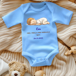 Ein hellblauer Baby-Body mit einem süßen Motiv eines schlafenden Babys. Darüber steht der Name 'Eva' in blauer Schrift. Darunter folgt der Text 'Frei, frech und fröhlich seit: 24.12.2023' in goldener und blauer Schrift. Der Body liegt auf einer beigen, gestrickten Decke, umgeben von Spielzeug, was eine warme und einladende Atmosphäre schafft. Ein schönes, personalisiertes Geschenk zur Geburt.