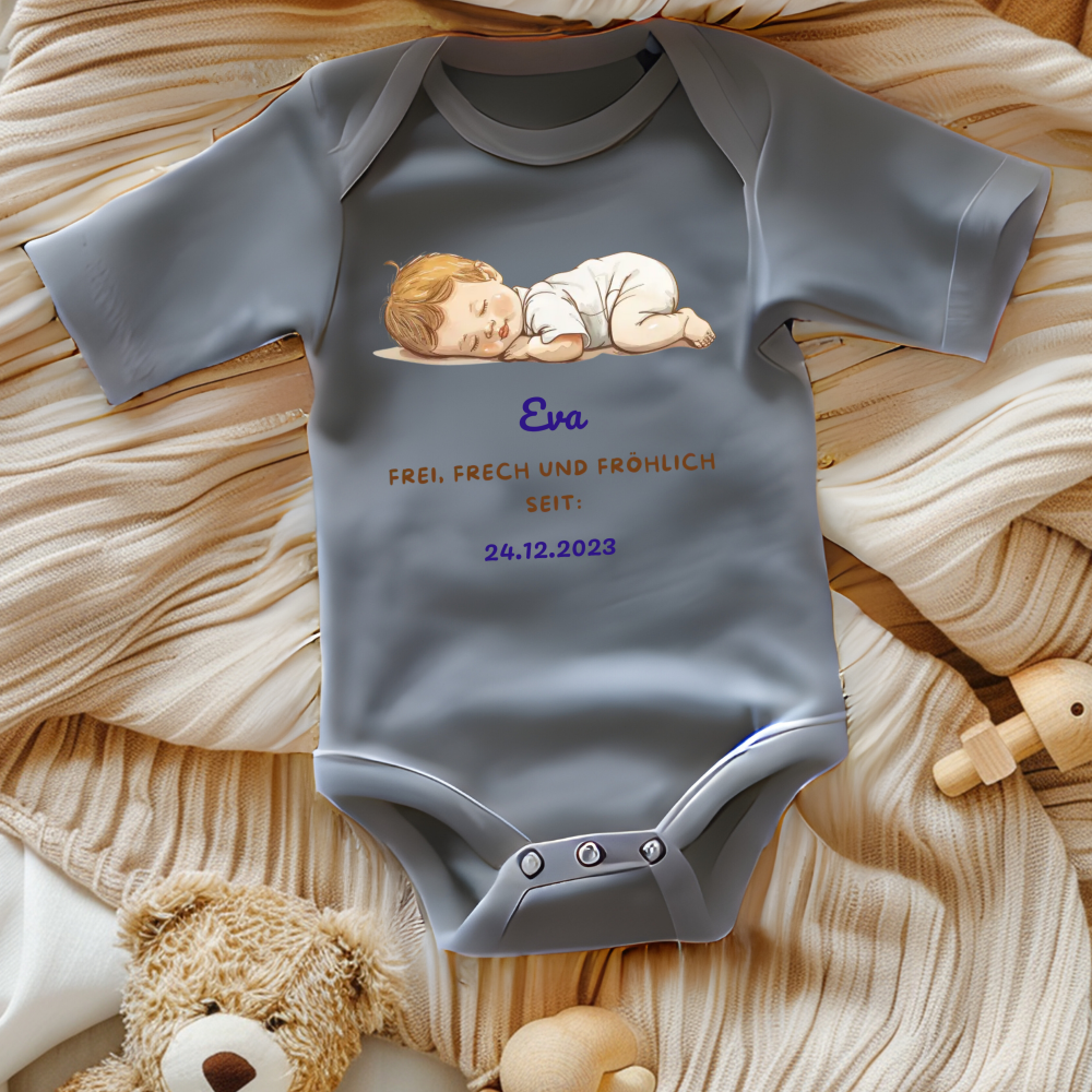 Ein grauer Baby-Body mit einem niedlichen Motiv eines schlafenden Babys. Darüber ist der Name 'Eva' in blauer Schrift abgebildet, gefolgt vom Text 'Frei, frech und fröhlich seit: 24.12.2023' in goldener und blauer Schrift. Der Body liegt auf einer beigen, gestrickten Decke und ist von Spielzeug umgeben, was eine warme und gemütliche Stimmung schafft. Ein individuelles und liebevolles Geschenk zur Geburt.