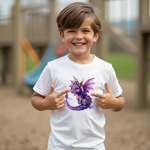 Ein lächelnder Junge steht draußen auf einem Spielplatz und trägt ein weißes T-Shirt mit einem lila Drachenmotiv. Der Junge zeigt mit beiden Zeigefingern auf das Drachenbild auf seinem T-Shirt und wirkt begeistert. Der Drache auf dem T-Shirt ist detailreich gestaltet, mit leuchtenden Augen, funkelnden Schuppen und glitzernden Flügeln, die in verschiedenen Lila- und Pinktönen gehalten sind. Im Hintergrund ist unscharf ein Klettergerüst zu sehen, was die spielerische Atmosphäre des Bildes unterstreicht.