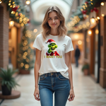 Alt-Text: Eine Frau trägt ein weißes T-Shirt mit einem humorvollen, weihnachtlichen Motiv. Auf der Vorderseite ist eine grüne Figur mit Weihnachtsmann-Mütze abgebildet, die direkt in die Kamera zeigt. Darunter steht in gelben Buchstaben der Text "I WANT YOU". Die Frau steht in einem festlich geschmückten Innenbereich, der eine warme, weihnachtliche Atmosphäre erzeugt.