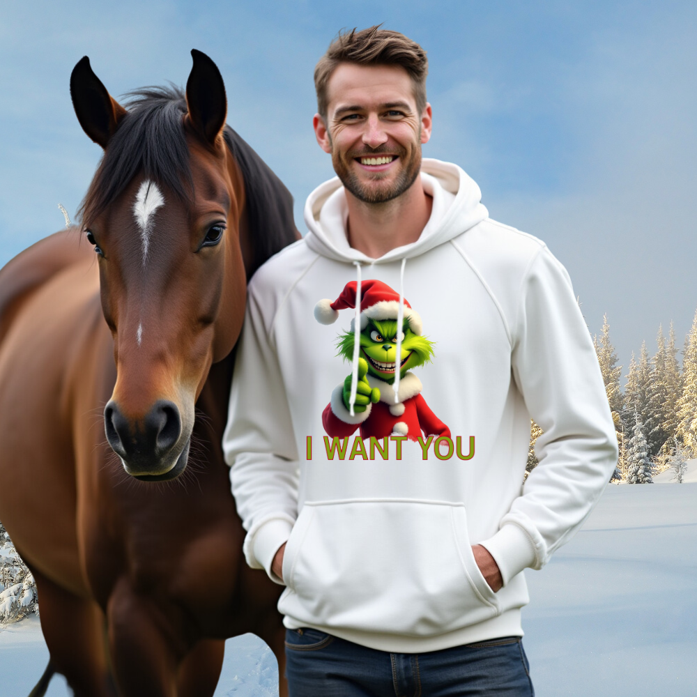 Ein Mann trägt einen weißen Hoodie mit einem humorvollen weihnachtlichen Motiv. Auf dem Hoodie ist eine grüne Grinch-Figur mit Weihnachtsmann-Mütze zu sehen, die direkt in die Kamera zeigt, darunter steht der Text "I WANT YOU". Der Mann steht neben einem braunen Pferd in einer winterlichen Landschaft, was eine gemütliche, festliche Stimmung schafft.