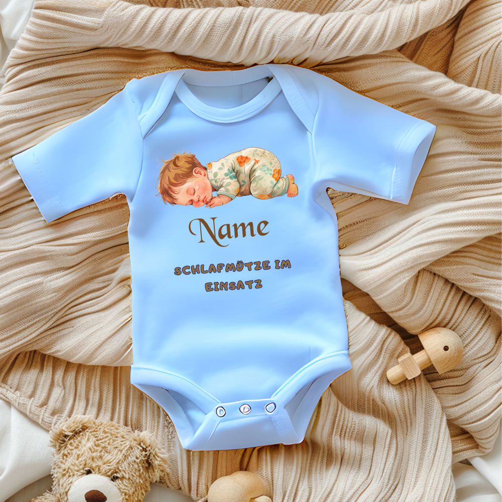 Ein hellblauer Baby-Body mit einem süßen Motiv eines schlafenden Babys in gemusterter Schlafkleidung. Darüber steht der personalisierbare Schriftzug 'Name' in brauner, verspielter Schrift. Darunter befindet sich der Text 'SCHLAFMÜTZE IM EINSATZ' in grauer, verspielter Schrift. Der Body liegt auf einer beigen, gestrickten Decke, umgeben von Spielzeug, was eine gemütliche und liebevolle Atmosphäre schafft. Ein perfektes, personalisierbares Geschenk für kleine Schlafmützen.