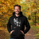 Ein Mann im schwarzen Hoodie mit einem stilisierten, geheimnisvollen Design. Das Design zeigt eine Person im Anzug und Zylinder, die Spielkarten in der Hand hält. Der Hintergrund zeigt einen herbstlichen Wald mit bunten Blättern, was eine warme und einladende Atmosphäre schafft.