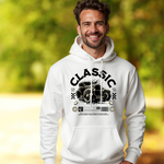 Ein Mann im weißen Hoodie mit einem klassischen Automobil-Design. Der Aufdruck zeigt ein detailliertes Vintage-Auto mit dem großen Schriftzug "Classic" darüber. Es sind auch dekorative Elemente wie Rennflaggen, Sterne und ein Barcode zu sehen, die den Retro-Stil verstärken. Darunter befindet sich ein kleiner Text, der den nostalgischen Charakter des Designs hervorhebt. Der Hintergrund zeigt eine unscharfe Naturkulisse, was dem Bild eine frische und entspannte Atmosphäre verleiht.