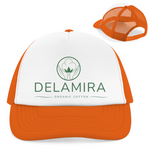 Eine orange und weiße Trucker-Cap mit Netzrückseite, auf der Vorderseite das grüne Delamira-Logo mit dem Schriftzug ‚Organic Cotton‘.