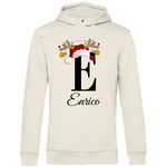 Ein cremefarbener Hoodie mit einem weihnachtlichen Design, das den Buchstaben "E" zeigt. Der Buchstabe ist in Schwarz gehalten und mit einem Weihnachtsmann-Hut sowie Rentiergeweihen verziert, an denen bunte Kugeln hängen. Unter dem Buchstaben ist der personalisierte Name "Enrico" in eleganter, geschwungener Schrift zu sehen. Der Hoodie strahlt eine festliche und personalisierte Stimmung aus und eignet sich perfekt für die Winter- und Weihnachtszeit.