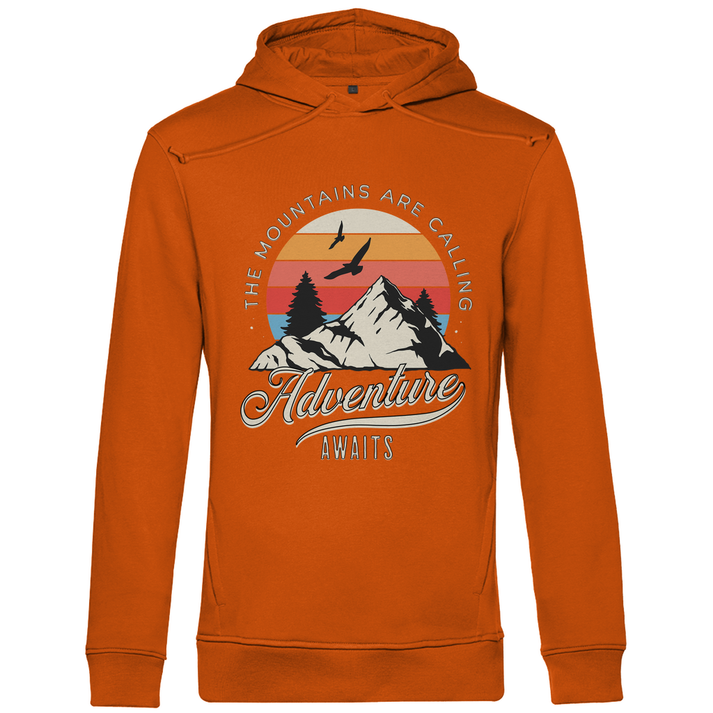 Ein oranger Hoodie mit einem Outdoor-Design, das einen Berg, Bäume und fliegende Vögel zeigt. Im Hintergrund ist ein Sonnenuntergang in warmen Farbstreifen abgebildet. Der Text "The Mountains Are Calling" ist im oberen Bereich des Designs zu sehen, während "Adventure Awaits" in geschwungener Schrift darunter steht. Das Design vermittelt eine abenteuerliche und naturverbundene Atmosphäre, ideal für Liebhaber von Outdoor-Aktivitäten und Bergen.