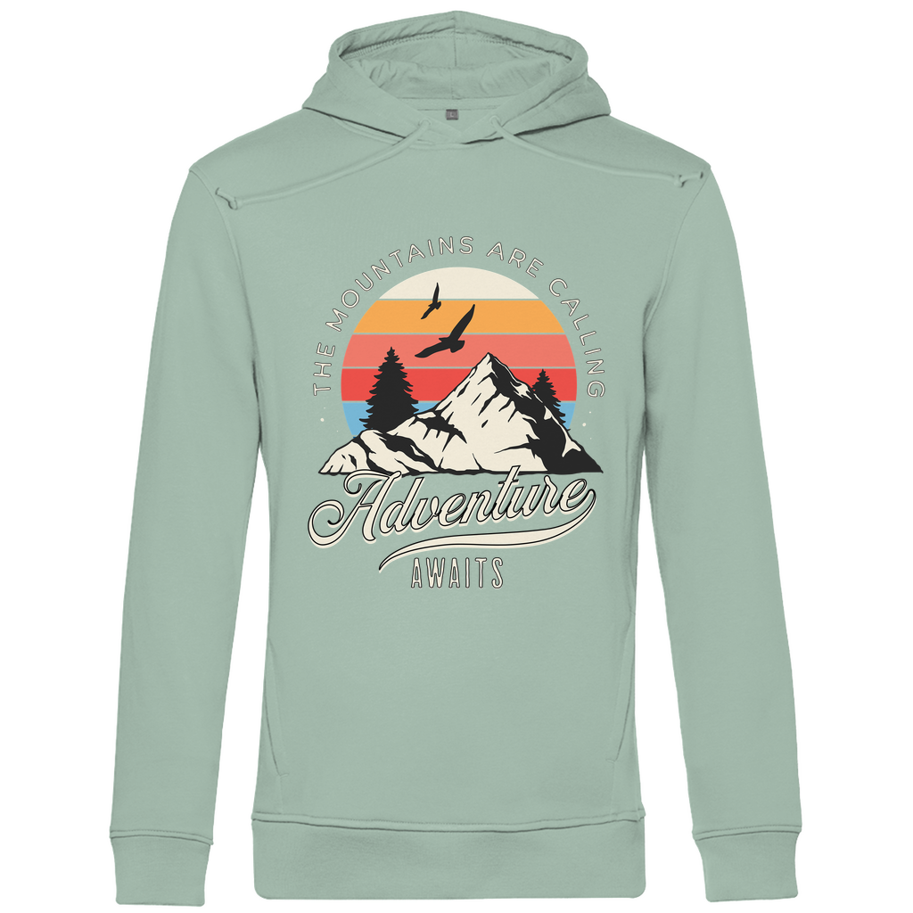 Ein hellgrüner Hoodie mit einem Outdoor-Design, das einen Berg, Bäume und fliegende Vögel zeigt. Im Hintergrund ist ein Sonnenuntergang in warmen Farbstreifen abgebildet. Der Text "The Mountains Are Calling" ist im oberen Bereich des Designs zu sehen, während "Adventure Awaits" in geschwungener Schrift darunter steht. Das Design vermittelt eine abenteuerliche und naturverbundene Atmosphäre, ideal für Liebhaber von Outdoor-Aktivitäten und Bergen.