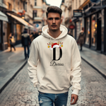 Ein cremefarbener Hoodie mit einem weihnachtlichen Design, das den Buchstaben "D" zeigt. Der Buchstabe ist in Schwarz gehalten und mit einem Weihnachtsmann-Hut sowie Rentiergeweihen verziert, an denen bunte Kugeln hängen. Unter dem Buchstaben ist der personalisierte Name "Darius" in eleganter, geschwungener Schrift zu sehen. Der Hoodie strahlt eine festliche und personalisierte Stimmung aus und eignet sich perfekt für die Winter- und Weihnachtszeit.