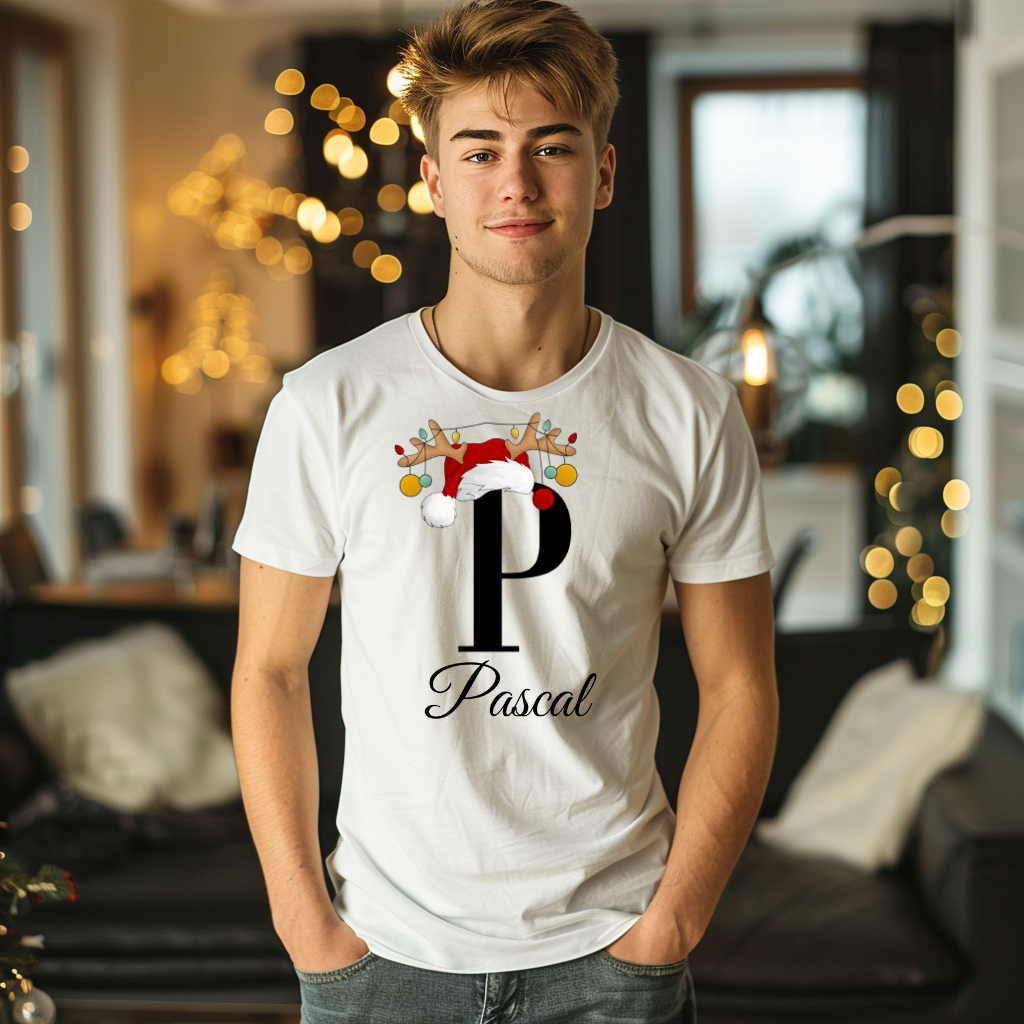 Ein junger Mann steht in einem gemütlichen, weihnachtlich dekorierten Raum, im Hintergrund sind Lichterketten und weihnachtliche Dekoration zu sehen. Er trägt ein weißes T-Shirt mit einem festlichen Design. Auf dem T-Shirt ist ein großer Buchstabe "P" abgebildet, der mit einem Weihnachtsmann-Hut und Rentiergeweihen dekoriert ist, an denen bunte Kugeln hängen. Unter dem Buchstaben steht der Name "Pascal" in eleganter, geschwungener Schrift. Das Design strahlt eine personalisierte und weihnachtliche Stimmung 