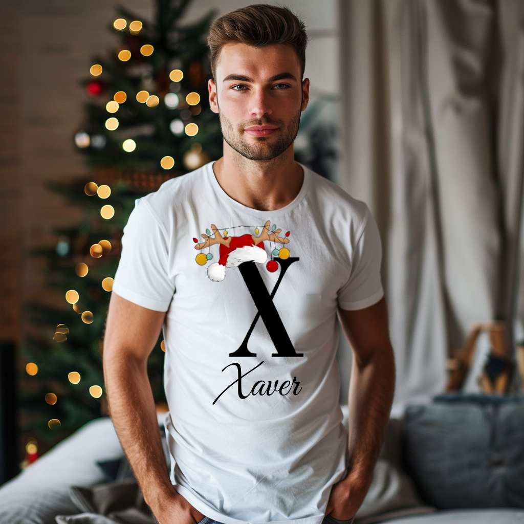 Ein junger Mann steht in einem weihnachtlich dekorierten Raum, im Hintergrund ist ein geschmückter Weihnachtsbaum mit Lichtern zu sehen. Er trägt ein weißes T-Shirt mit einem festlichen Design. Auf dem T-Shirt ist ein großer Buchstabe "X" abgebildet, der mit einem Weihnachtsmann-Hut und Rentiergeweihen dekoriert ist, an denen bunte Kugeln hängen. Unter dem Buchstaben steht der Name "Xaver" in eleganter, geschwungener Schrift. Das Design vermittelt eine personalisierte und festliche Stimmung.