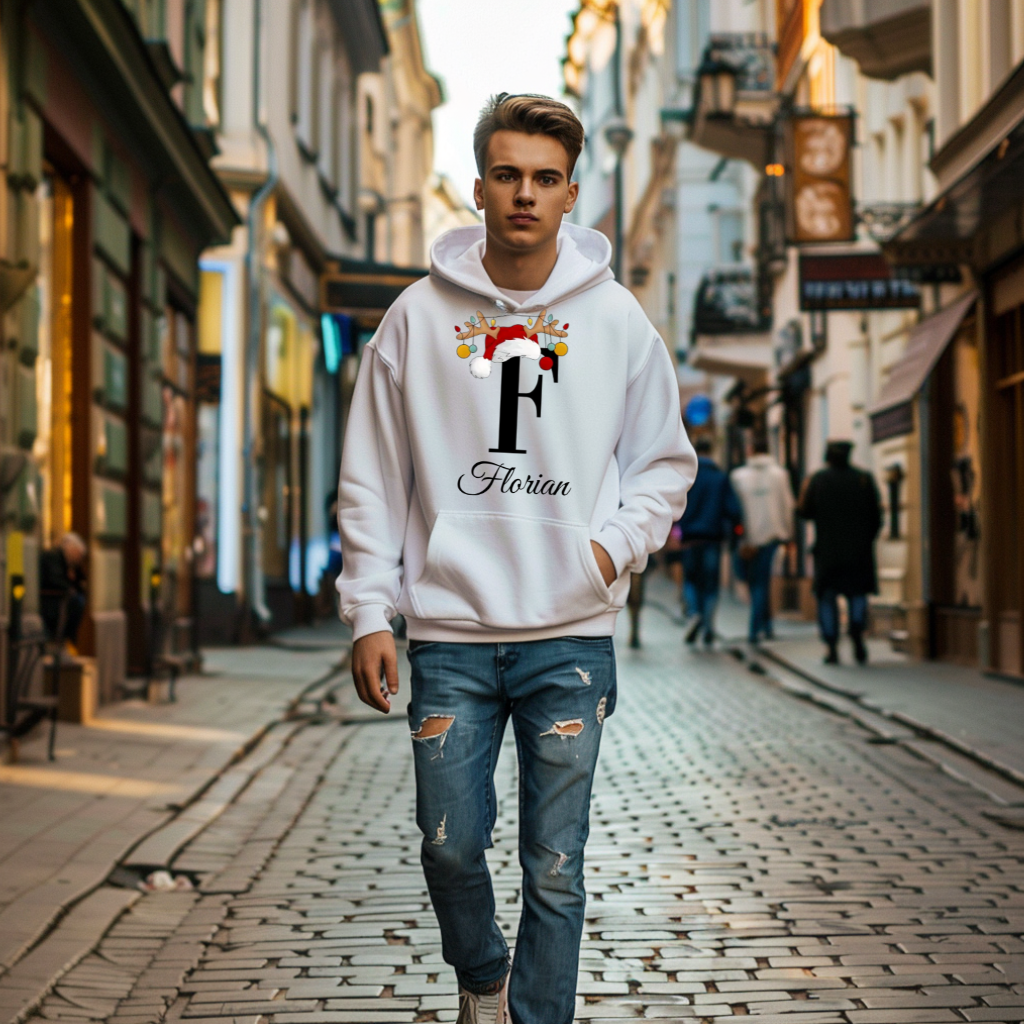 Ein junger Mann trägt einen weißen Hoodie mit einem weihnachtlichen Design. Das Design zeigt den Buchstaben "F", der schwarz gehalten ist und von einem Weihnachtsmann-Hut sowie Rentiergeweihen geschmückt wird, an denen bunte Kugeln hängen. Unter dem Buchstaben ist der personalisierte Name "Florian" in eleganter, geschwungener Schrift abgebildet. Der Hoodie vermittelt eine festliche und persönliche Stimmung, passend zur Weihnachtszeit.