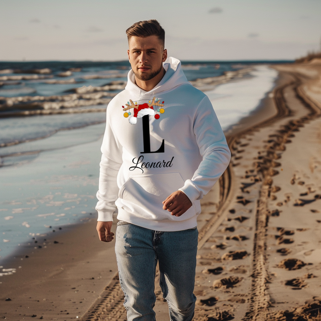 Ein junger Mann spaziert am Strand entlang und trägt einen weißen Hoodie mit weihnachtlichem Design. Der Buchstabe „L“ ist in Schwarz groß auf der Brust abgebildet und mit einem Weihnachtsmannhut sowie Rentiergeweihen verziert, an denen bunte Kugeln hängen. Darunter steht der Name „Leonard“ in eleganter, geschwungener Schrift. Der Hoodie vermittelt eine festliche und gleichzeitig personalisierte Atmosphäre, ideal für die kalten Wintertage.