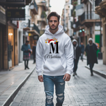 Dieses Bild zeigt einen jungen Mann, der einen weißen Hoodie mit einem festlichen Weihnachtsdesign trägt. Der Hoodie ist mit einem großen schwarzen Buchstaben „M“ bedruckt, der mit einer Weihnachtsmütze und einem Rentiergeweih verziert ist, an dem bunte Kugeln hängen. Unter dem Buchstaben steht in eleganter Schrift der Name „Matthias“. Der Hoodie strahlt eine weihnachtliche Atmosphäre aus und passt perfekt zur festlichen Jahreszeit.