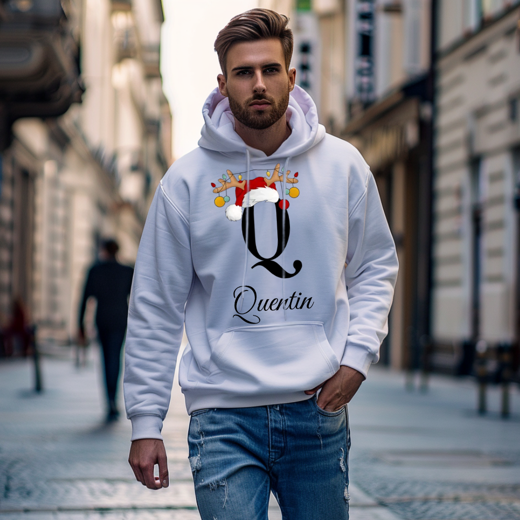 Das Bild zeigt einen jungen Mann, der einen weißen Hoodie trägt, auf dem ein großes „Q“ abgebildet ist, dekoriert mit einer Weihnachtsmütze und einem Rentiergeweih, an dem bunte Kugeln hängen. Darunter ist der Name „Quentin“ in einer eleganten, geschwungenen Schrift zu sehen. Der Hoodie vermittelt eine festliche Stimmung und eignet sich perfekt für die Weihnachtszeit.