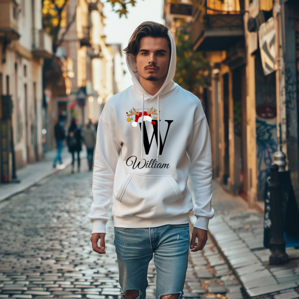 Weißer Hoodie mit weihnachtlichem Design, der den Buchstaben „W“ in Schwarz zeigt. Der Buchstabe ist mit einem Weihnachtsmann-Hut und Rentiergeweihen verziert, an denen bunte Kugeln hängen. Darunter steht der Name „William“ in eleganter, geschwungener Schrift. Der Hoodie strahlt eine festliche und personalisierte Atmosphäre aus, ideal für die Weihnachtszeit. Der Träger läuft durch eine gepflasterte Straße in einer städtischen Umgebung.