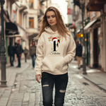 Auf dem Bild ist eine junge Frau zu sehen, die einen weißen Hoodie trägt. Auf dem Hoodie ist ein festliches Design mit einem großen schwarzen Buchstaben sowie der Namen „Felicitas“ passend zum Buchstaben, in eleganter Schrift gedruckt. Über dem Buchstaben sind ein Rentiergeweih, ein Weihnachtsmann-Hut und bunte Kugeln als weihnachtliche Dekoration angebracht. Die Frau steht in einer belebten, unscharf abgebildeten Stadtstraße mit Lichtern und Menschen im Hintergrund, mit einer winterlichen, Atmosphäre. 