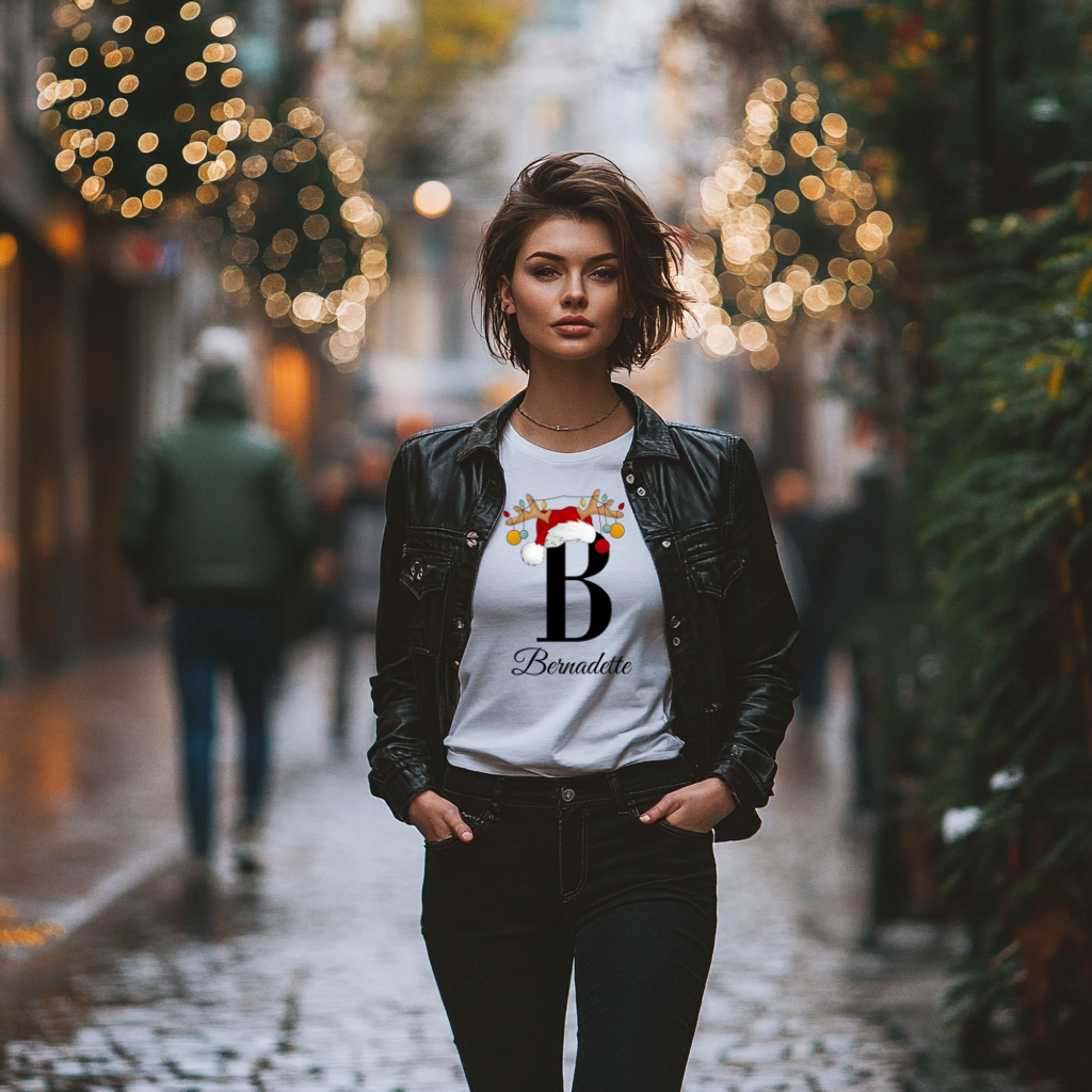 Ein weißes T-Shirt mit einem festlichen Weihnachtsmotiv. Der Buchstabe ‚B‘ ist in Schwarz dargestellt und mit einem Weihnachtsmann-Hut sowie Rentiergeweihen verziert, an denen bunte Kugeln hängen. Darunter ist der Name ‚Bernadette‘ in einer eleganten, geschwungenen Schrift zu sehen. Das T-Shirt strahlt eine persönliche und weihnachtliche Atmosphäre aus.