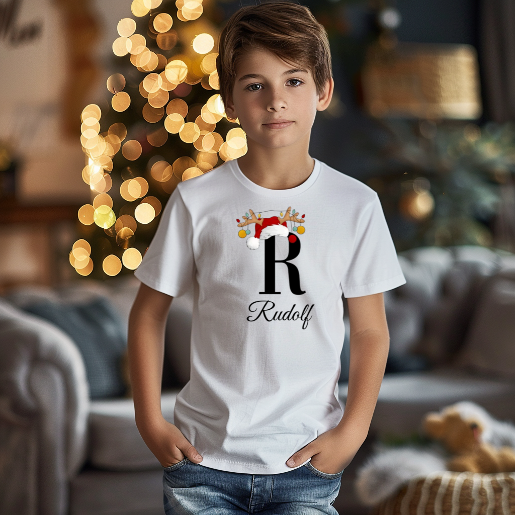 Weißes T-Shirt mit einem weihnachtlichen Design. Der große Buchstabe ‚R‘ ist in Schwarz aufgedruckt und wird von einem Weihnachtsmann-Hut sowie Rentiergeweihen mit bunten Kugeln geschmückt. Darunter steht der Name ‚Rudolf‘ in eleganter, geschwungener Schrift.