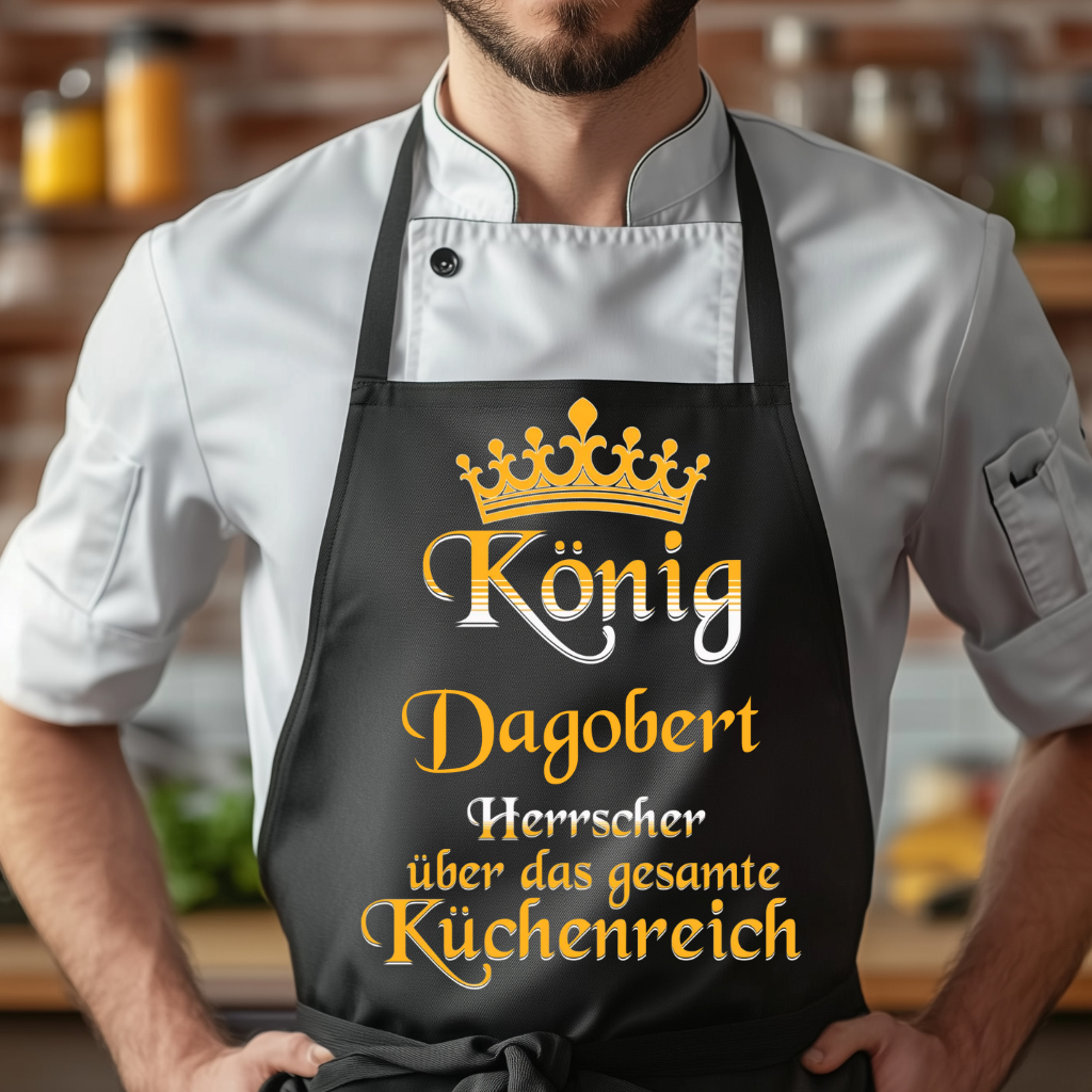 Ein Mann trägt eine schwarze Grillschürze mit einer goldenen Krone und dem personalisierten Schriftzug 'König [Name], Herrscher über das gesamte Küchenreich' in eleganter Schrift. Die Schürze hat eine praktische Tasche auf der Vorderseite. Der Mann trägt eine weiße Kochjacke, und im Hintergrund ist eine warme, gemütliche Kücheneinrichtung zu sehen.